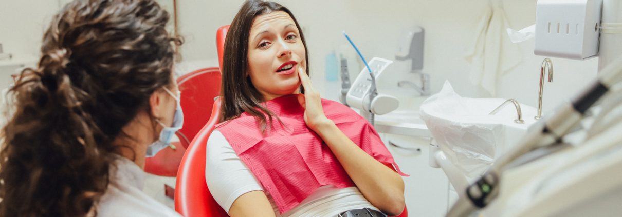Close-up portrait of a sad young girl with a painful tooth, a doctor in office chairs, an isolated dentist office background clinic.